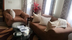 Un salon avec un canapé marron, une table basse en verre et un tapis à motifs.