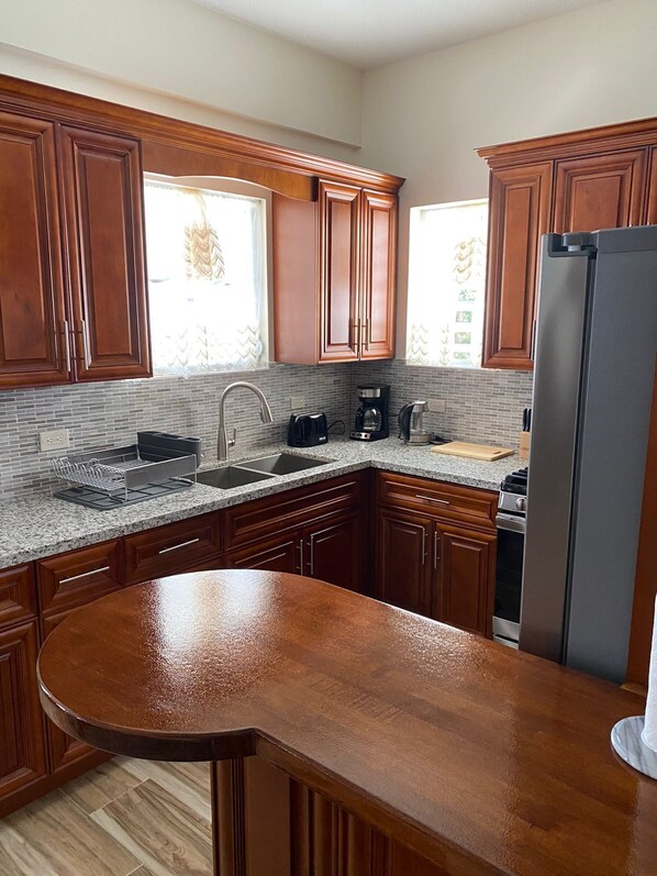 A kitchen with wooden cabinets, a granite countertop, a stainless steel refrigerator, and a built-in oven.