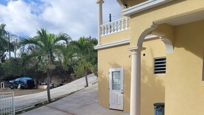 Un bâtiment jaune avec une porte blanche, un balcon et une poubelle.