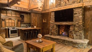 Ein rustikaler Innenraum mit Kamin aus Stein, einer Holzbar und einer Küche mit integriertem Backofen.