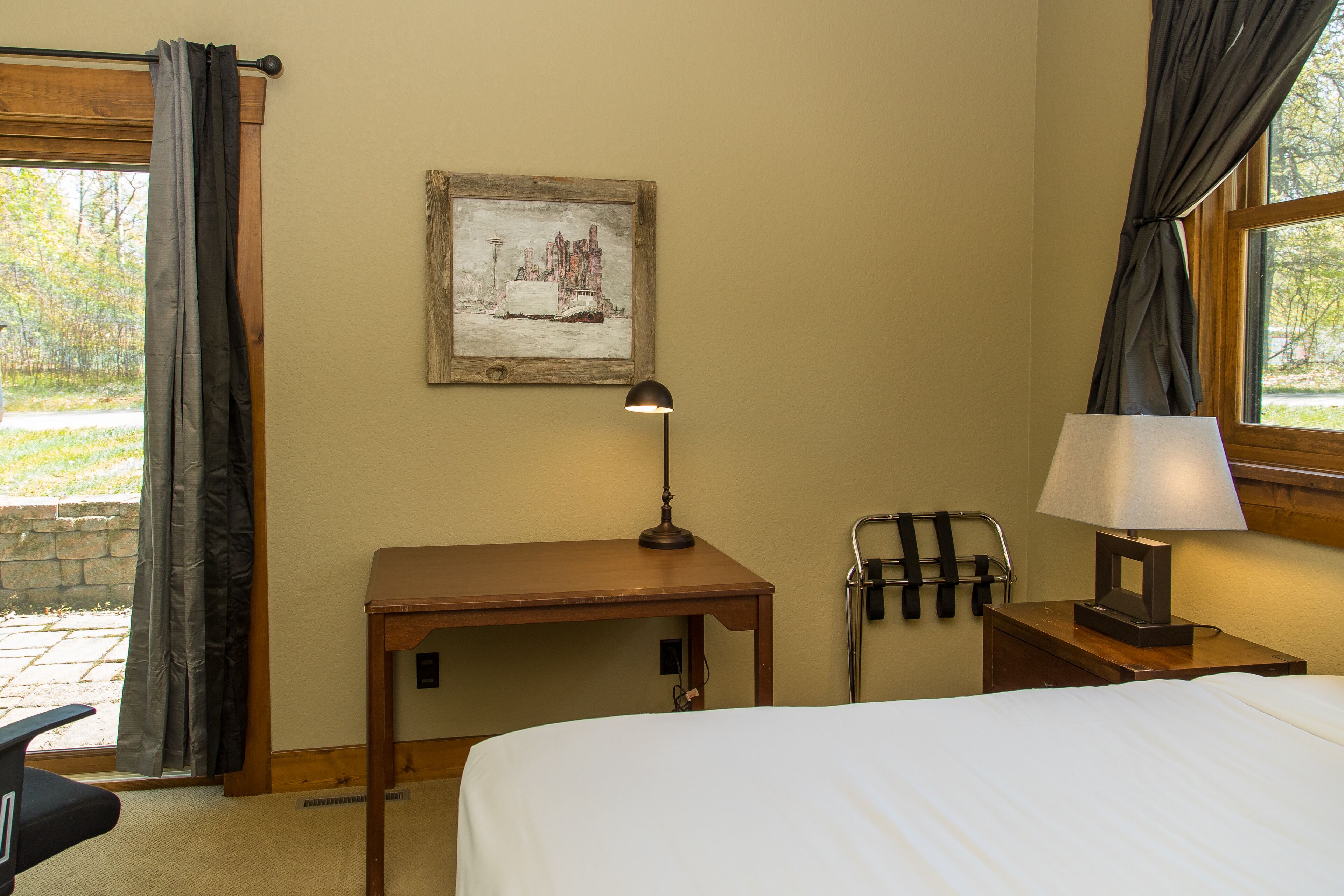 A hotel room with a bed, a desk, a lamp, a picture on the wall, and a window with curtains.