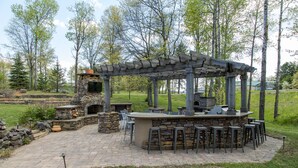 Ein Außenbereich mit Bar, Steinmauern, einem Kamin aus Stein und einer Holzpergola.