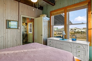 Quarto com cama, penteadeira e janela com vista para casas.