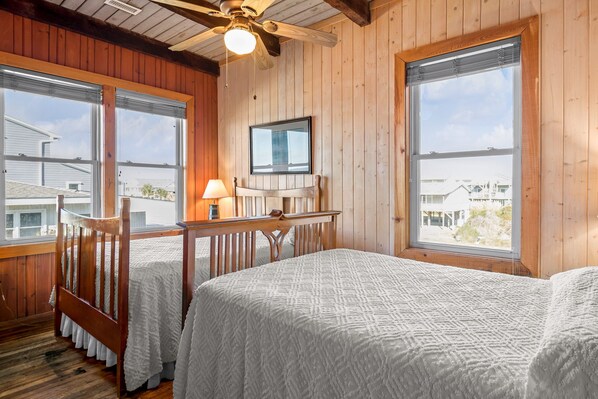A wooden cabin bedroom with two beds, a ceiling fan, and large windows offering a view of the surrounding area.