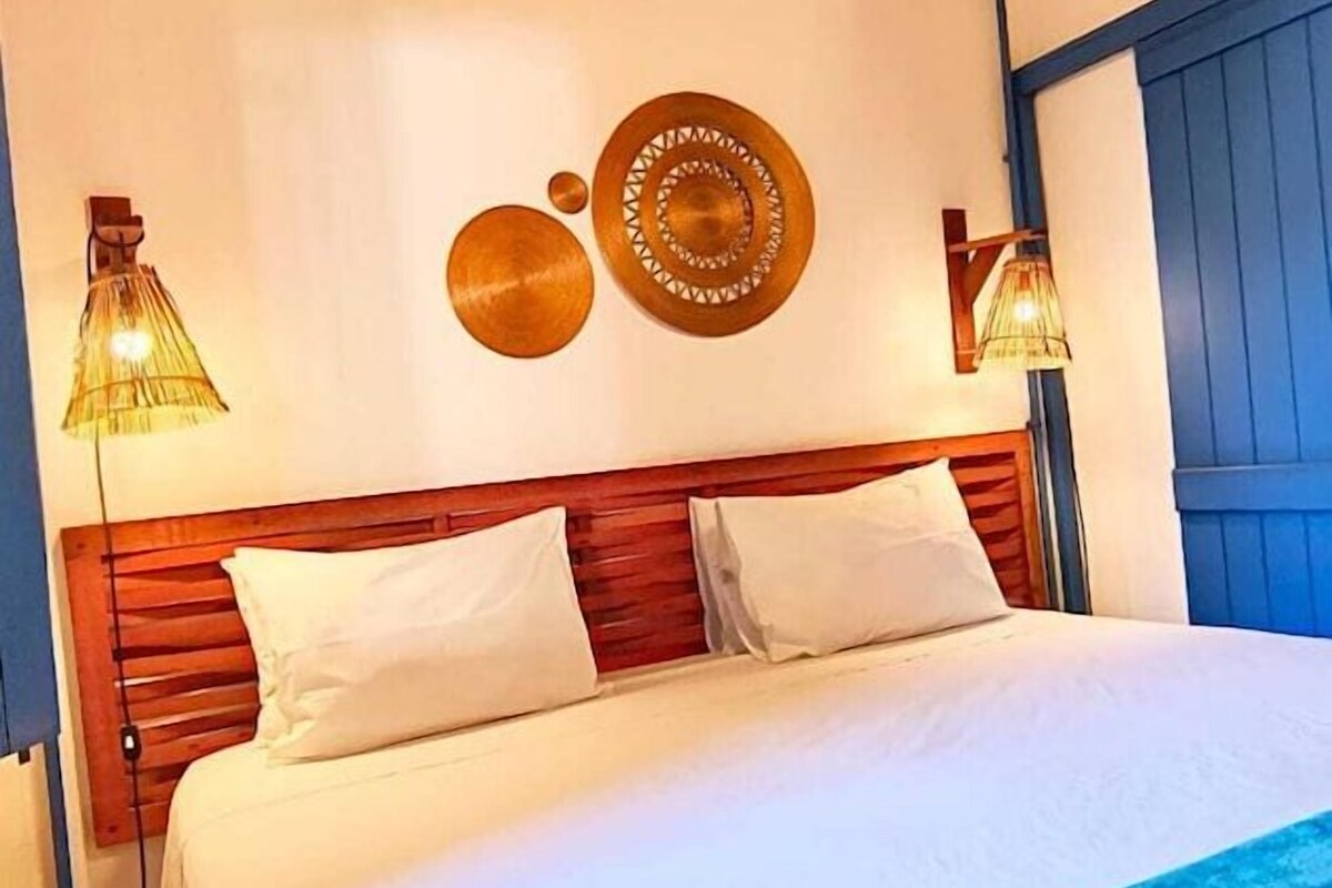 Un dormitorio con techo de madera, cama con ropa blanca y dos lámparas fijadas a la pared.