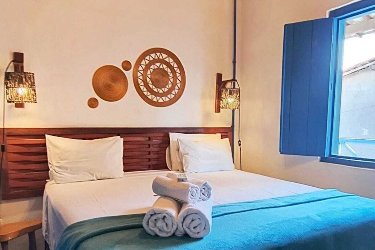Una habitación de hotel con una cama, lámparas de noche, un adorno en la pared y una ventana.