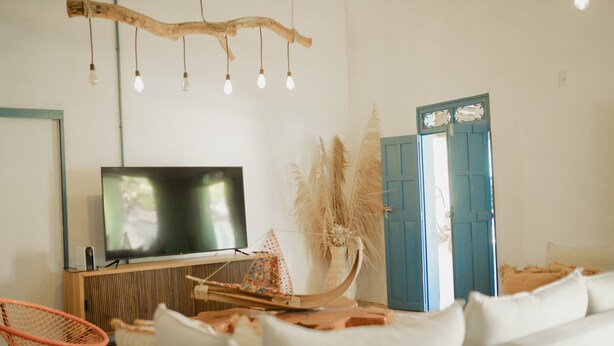 Una sala de estar con un televisor de pantalla plana, un mueble de madera, un sofá blanco, un colgante de techo y una puerta azul.