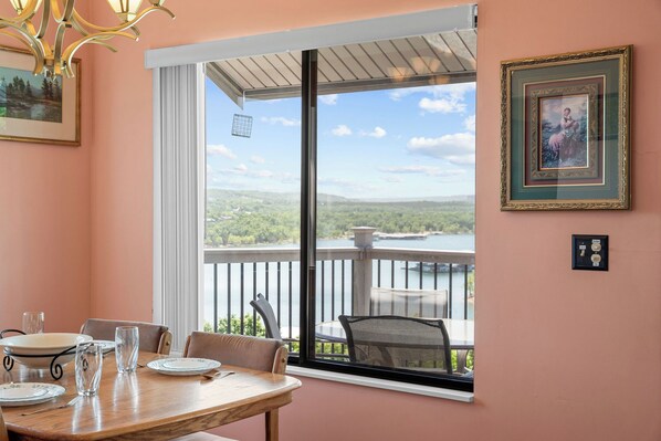 A dining area with a table set for four, a window with a view of a lake and hills, and a framed picture on the wall. - Best-View 3-Bedroom Condo, Close to Silver Dollar City with Free Tickets & Outdoor Pool (Branson)