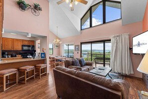 A spacious living area with a high ceiling, a kitchen with wooden cabinets, a dining area, and a balcony with a view. - Best-View 3-Bedroom Condo, Close to Silver Dollar City with Free Tickets & Outdoor Pool (Branson)