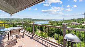Un balcon avec une table et des chaises, donnant sur un lac et une végétation luxuriante.