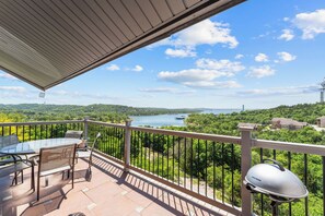 A balcony with a table and chairs, overlooking a lake and greenery.