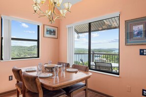 A dining area with a table set for four, large windows offering a view of a lake and hills, and a chandelier above.