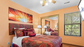 Une chambre avec un grand lit, un ventilateur de plafond, une fenêtre avec des stores et des œuvres d’art accrochées aux murs.