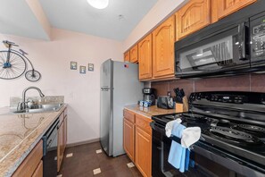 A compact kitchen with wooden cabinets, a refrigerator, a microwave, a stove, and a sink.