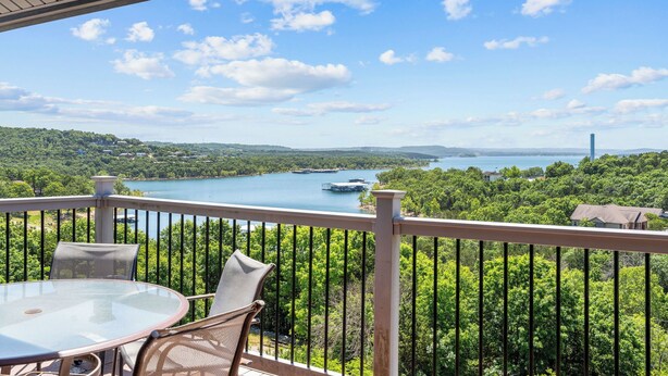 Un balcon avec une table et des chaises, donnant sur un lac où l’on peut voir des bateaux et, au loin, le paysage urbain.