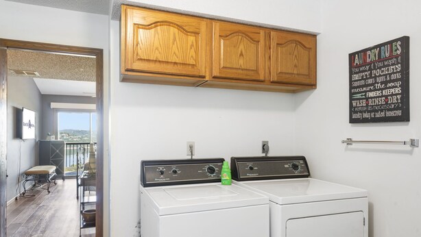 Una lavanderia con due lavatrici e asciugatrici, pensili in legno e un cartello con le regole per il bucato.