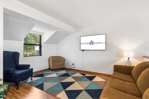 A living room with a TV mounted on the wall, a blue armchair, a brown sofa, and a patterned rug.