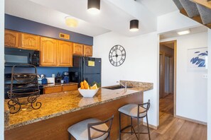 A modern kitchen with wooden cabinets, a stainless steel refrigerator, a coffee maker, and a clock on the wall.