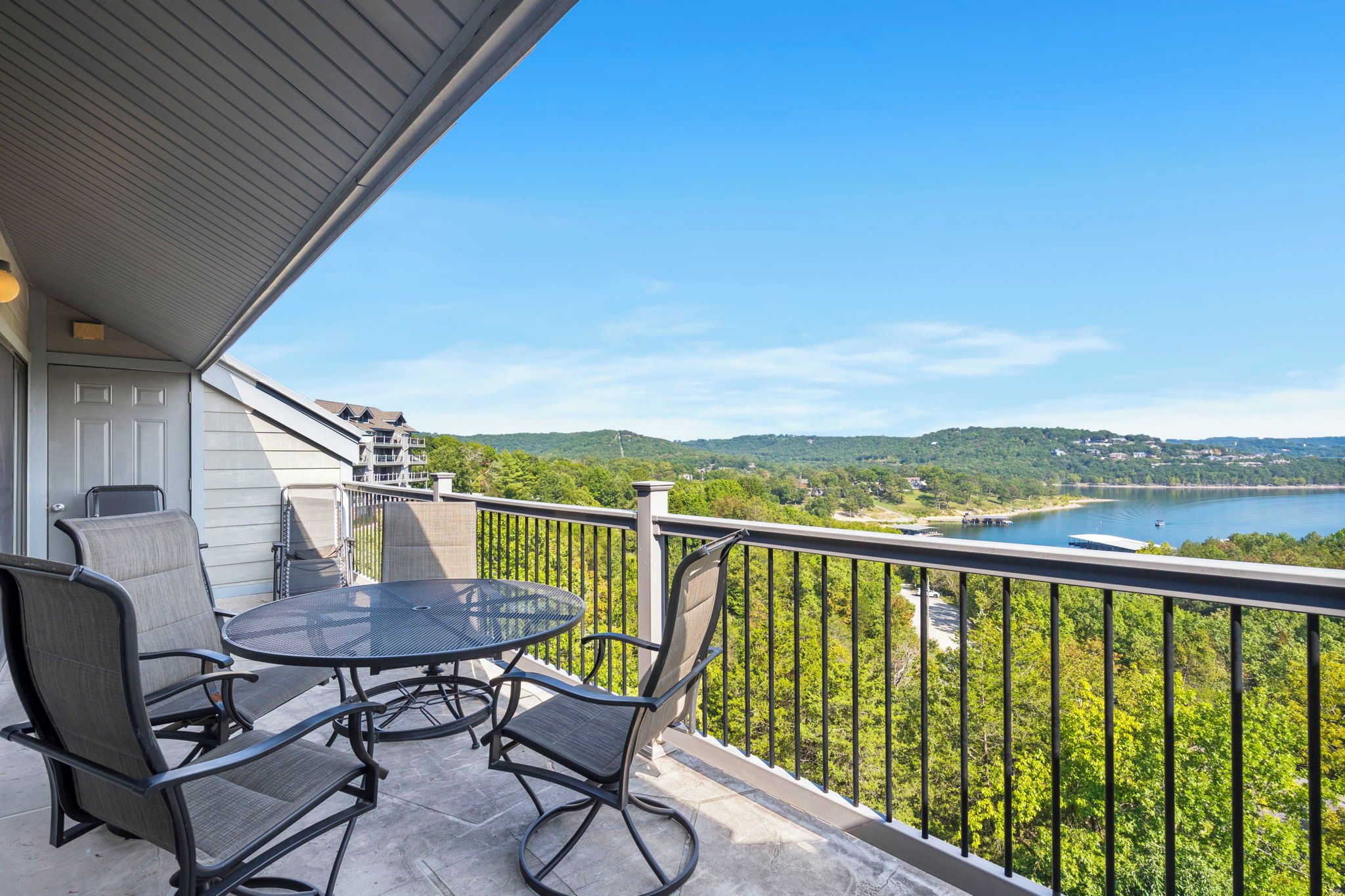 A balcony with a table and chairs, overlooking a lake and forested hills.