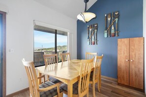 A dining area with a wooden table and chairs, a hanging light fixture, and a view through a window.