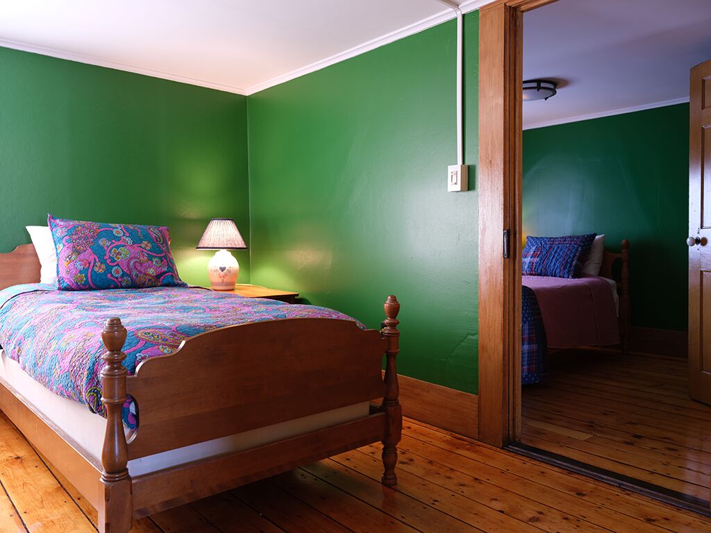 A bedroom with a wooden bed, green walls, and a wooden floor.