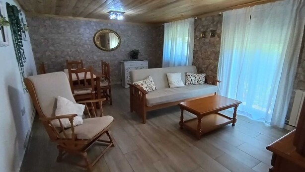 A living room with a sofa, two wooden chairs, a coffee table, a round mirror, and a stone wall. - La Caseta Rural House (La Casa De La Noguera)