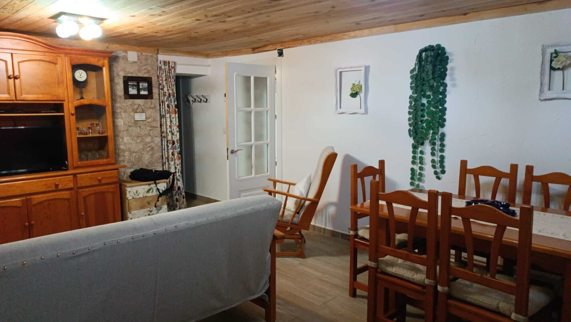 A dining area with wooden chairs and a table, a wooden cabinet with glass doors, and a stone wall.