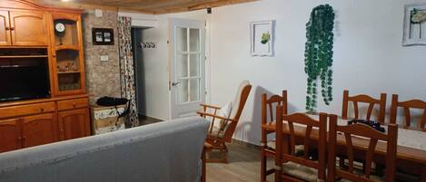A dining area with wooden chairs and a table, a wooden cabinet with glass doors, and a stone wall.