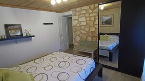 A bedroom with a bed, a chair, a mirror, and a stone wall. - La Caseta Rural House (La Casa De La Noguera)