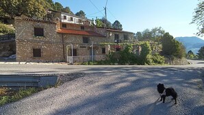 A stone building with a tiled roof, a gravel road, and a dog on a leash. - La Caseta Rural House (La Casa De La Noguera)