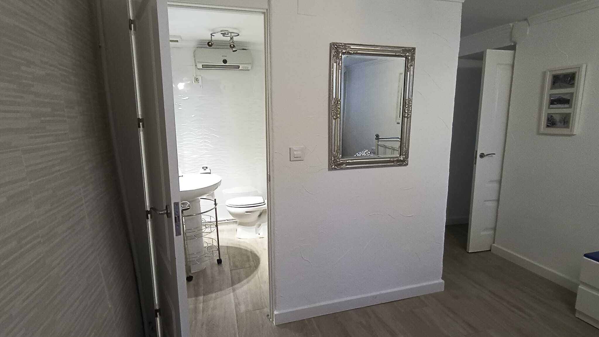 A hallway leading to a bathroom with a toilet, sink, and a mirror on the wall.