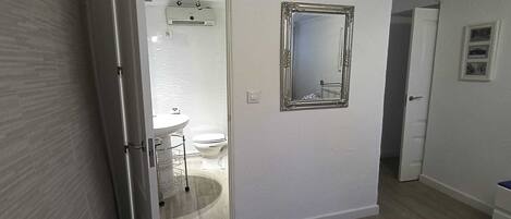 A hallway leading to a bathroom with a toilet, sink, and a mirror on the wall.