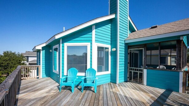 A turquoise building with a wooden deck, two chairs, and a glass door. - Short walk to Beach with Pool, Game Room, and Spa! (Corolla)