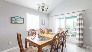 A dining area with a glass-top table, wooden chairs, and a chandelier. - Short walk to Beach with Pool, Game Room, and Spa! (Corolla)