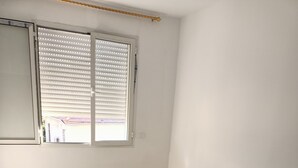 A bedroom with a bed, a window with blinds, and a tiled floor.