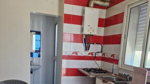 A compact kitchen with red and white tiles, a gas stove, a sink, and a window with blinds.