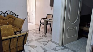A room with a sofa, a chair, and a table. There is a door and a wall-mounted TV.