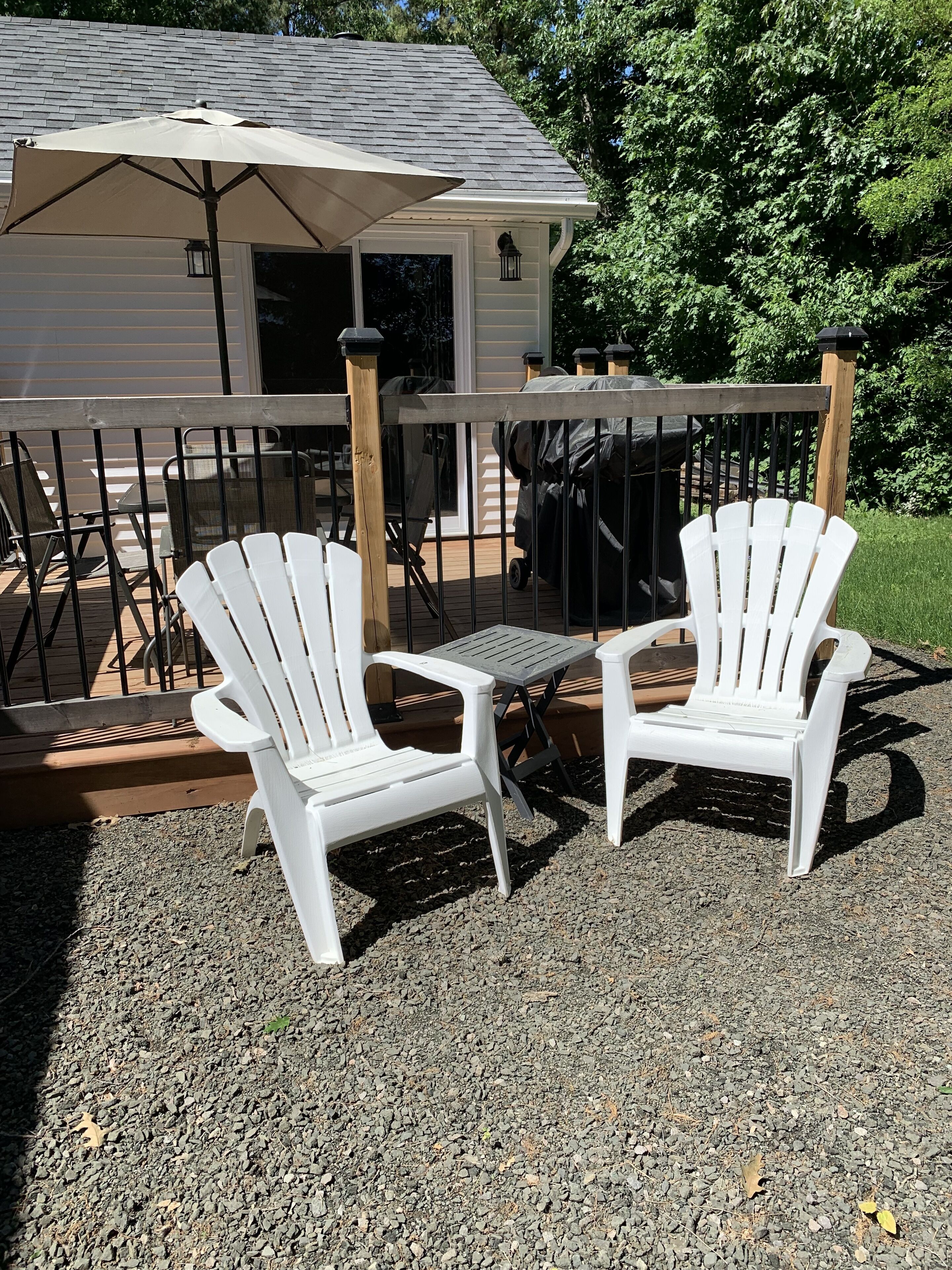 Deux chaises Adirondack blanches sont placées sur une terrasse en gravier, qui donne sur une plateforme en bois et est bordée d’une rambarde en métal.