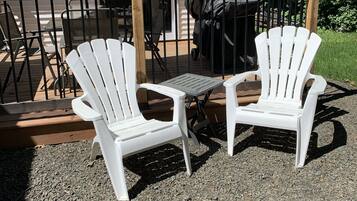 Deux chaises Adirondack blanches sont placées sur une terrasse en gravier, qui donne sur une plateforme en bois et est bordée d’une rambarde en métal.