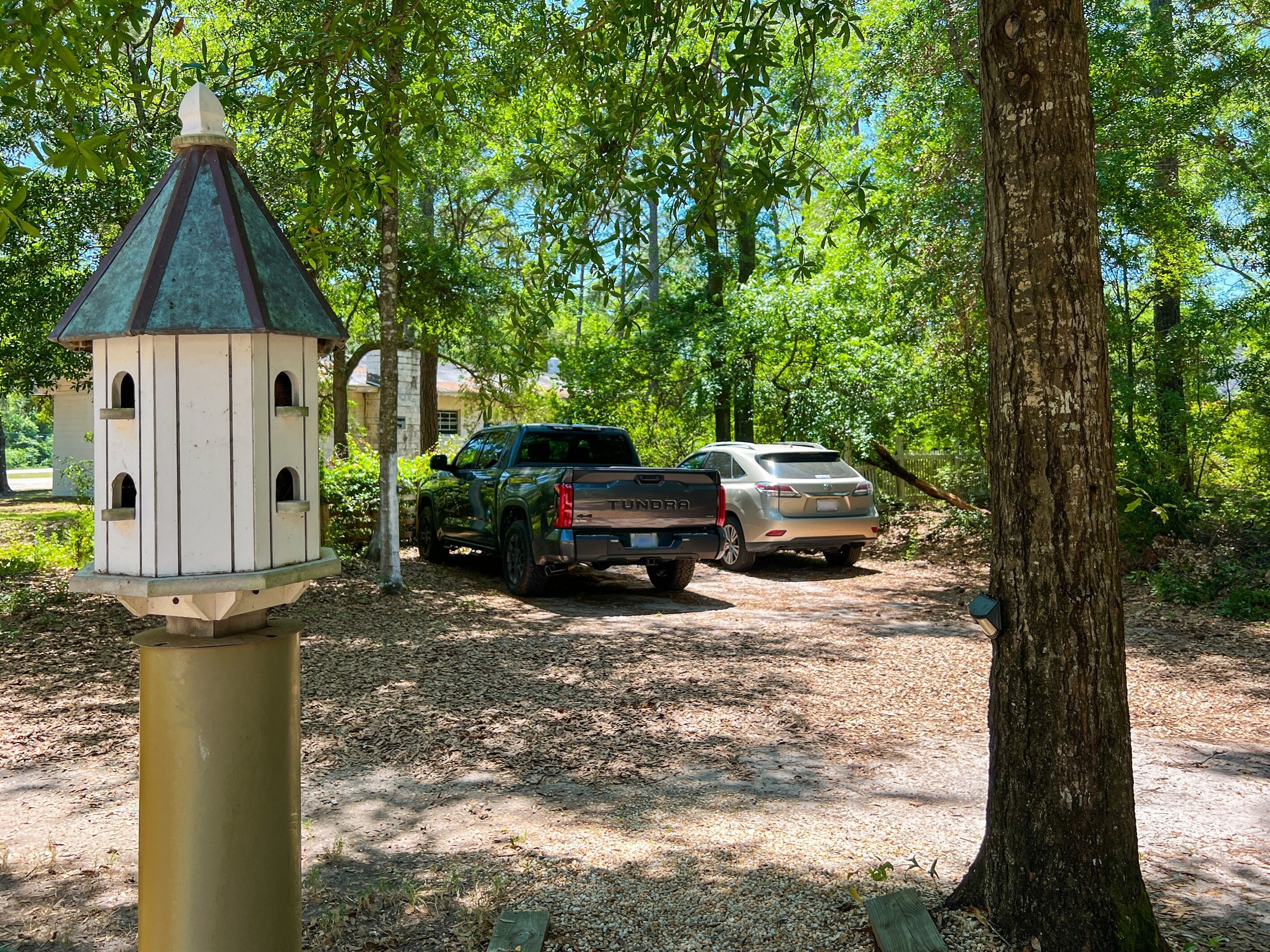 A parking area with two vehicles, a birdhouse, and a tree.