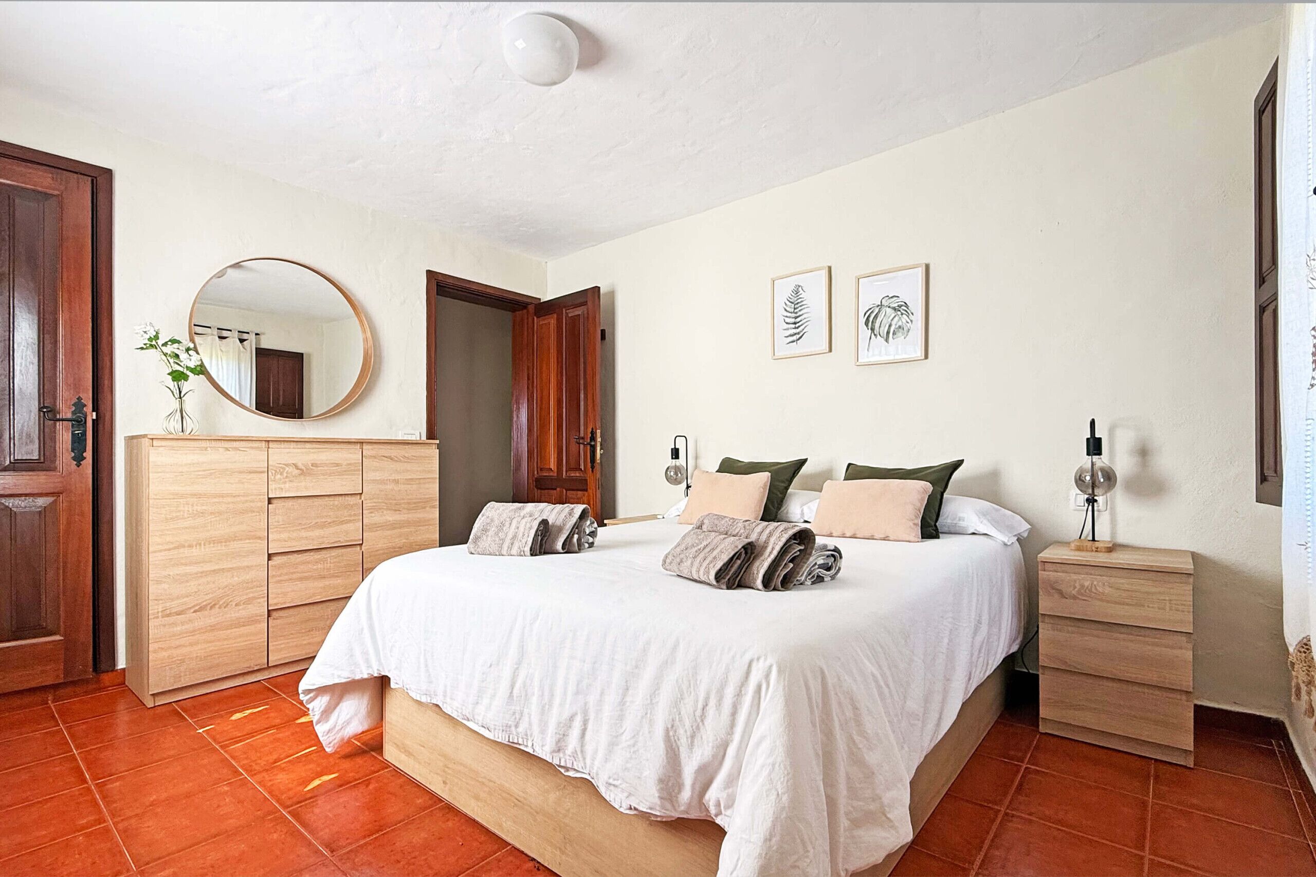 Une chambre à coucher comprenant un lit, une armoire en bois, une table de chevet et un miroir.