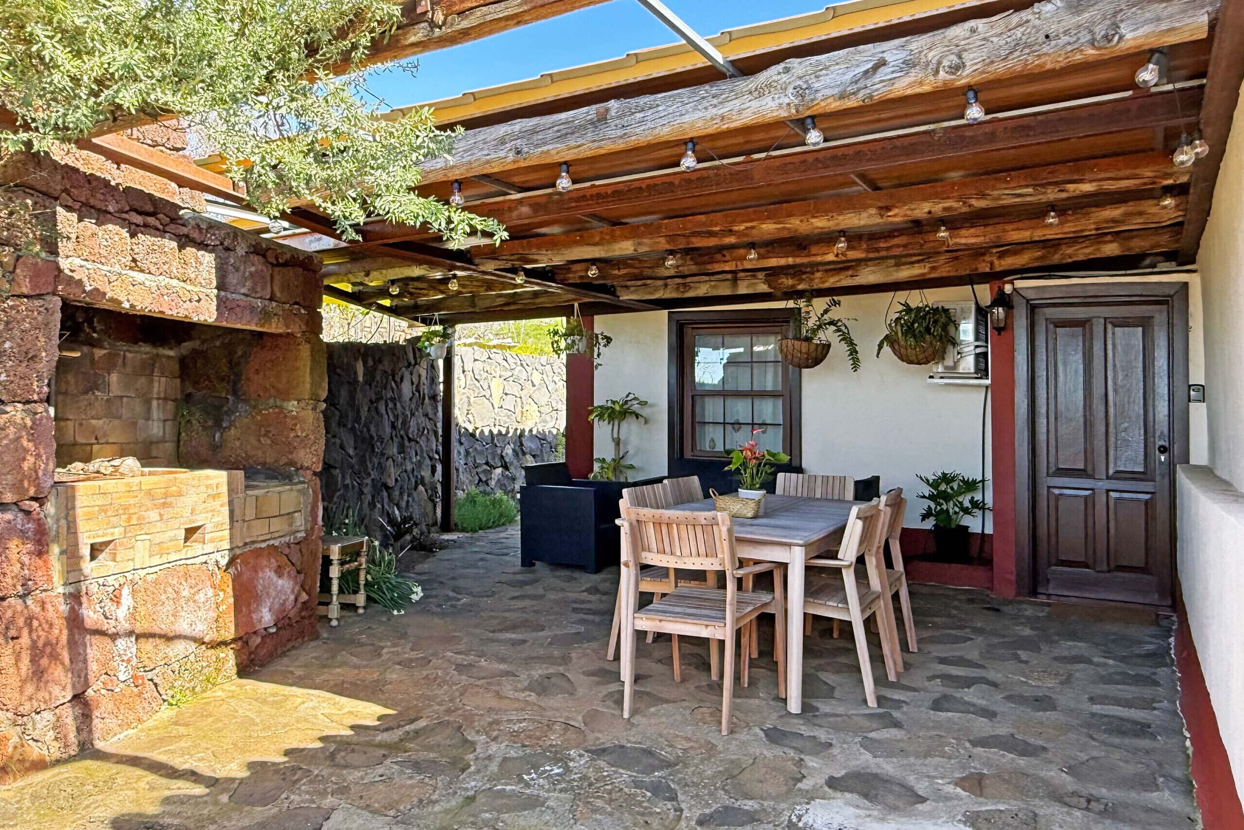Un patio couvert avec un sol en pierre, des meubles en bois et un mur en pierre.
