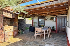 A covered patio with stone flooring, wooden furniture, and a stone wall.