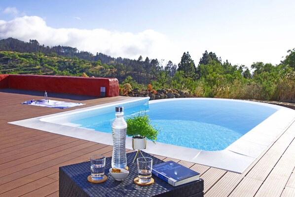A swimming pool with a wooden deck, a bottle, glasses, and a book.