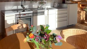 Et moderne køkken med hvide skabe, en stålvask og et spiseområde med en fletstol og en vase med blomster.