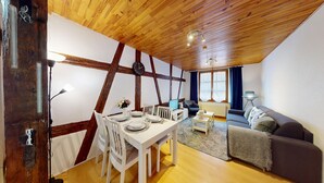 Een kamer met een houten plafond, een eettafel met borden en stoelen, een bank, een lamp en een raam met gordijnen.