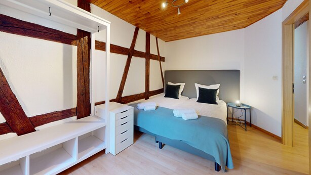 Een slaapkamer met een bed, nachtkastje en een houten plafond.