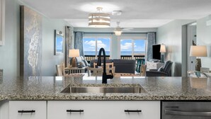 A modern kitchen with granite countertops, a stainless steel sink, and a dining area with a view of the ocean. - π 3BR/3BA π Ground Floor @ Pinnacle Port βοΈ π 50 π©΄π©΄ to the sand (Panama City Beach)