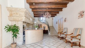 Un hall d’entrée spacieux avec une cheminée en pierre, un comptoir d’accueil en bois, une plante en pot et un escalier menant aux étages supérieurs.