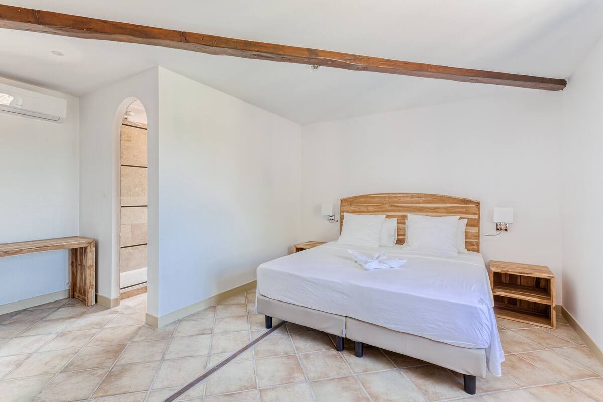 Een slaapkamer met een bed, een houten hoofdbord, nachtkastjes en een bankje.